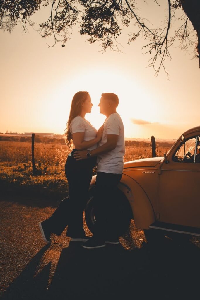 A couple embraces next to a vintage car during a beautiful sunset.